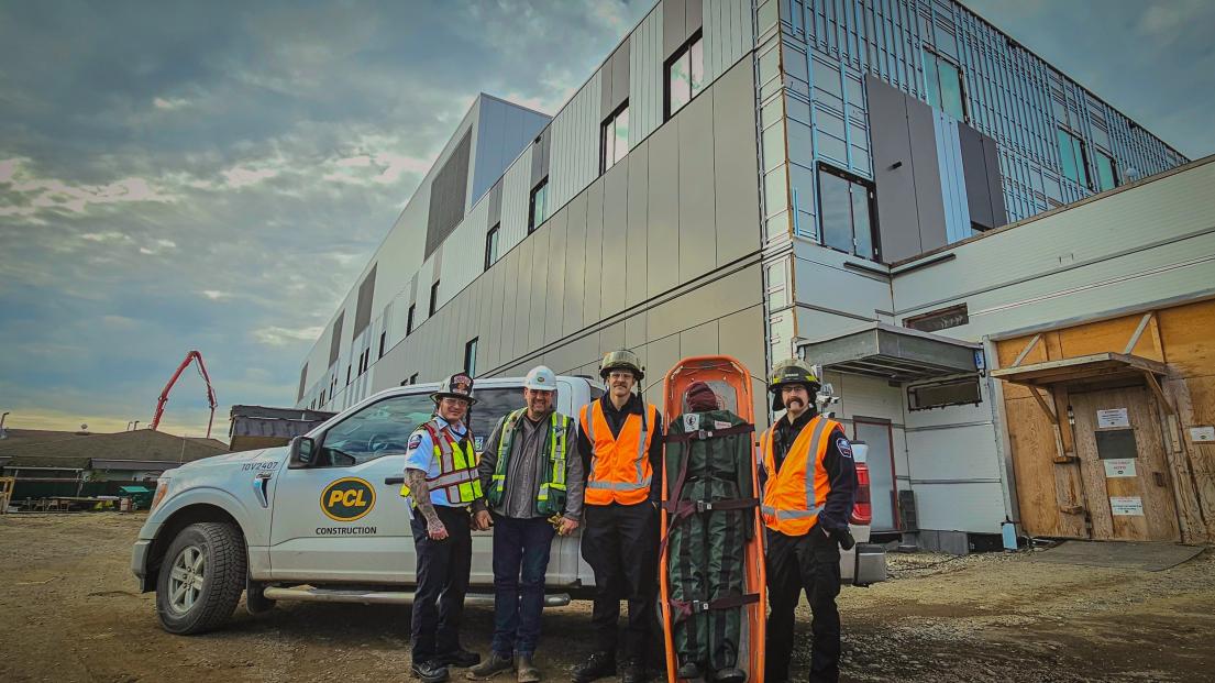 representatives from PCL Construction Management Inc and the Terrace Fire Department stand alongside the new rescue manikin, with a PCL truck and building in the background