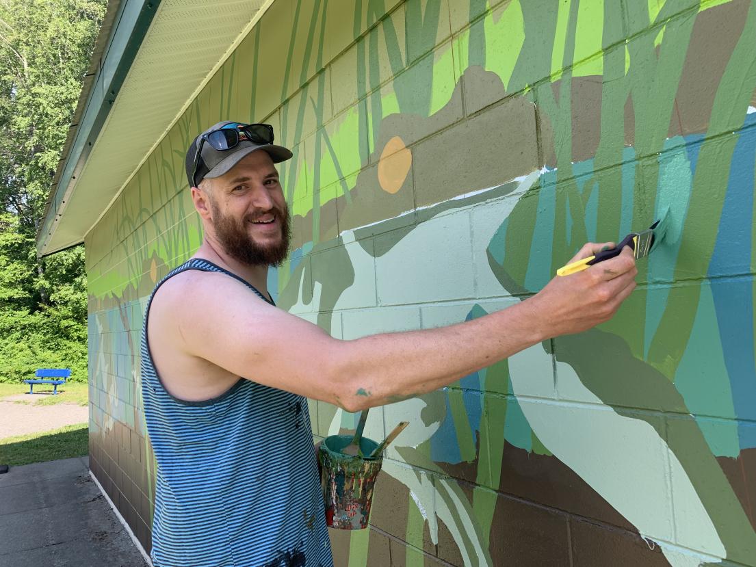 Artist painting mural on washrooms at Ferry Island